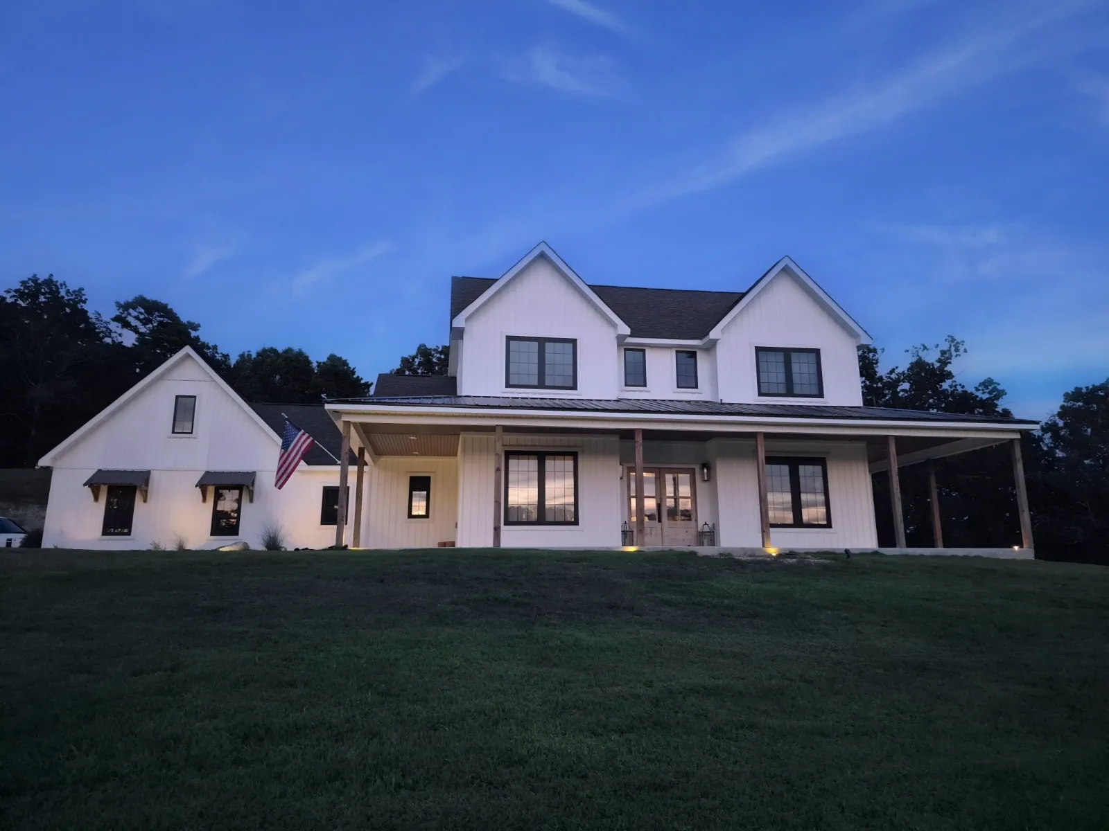 White modern farmhouse at twilight with lit windows.